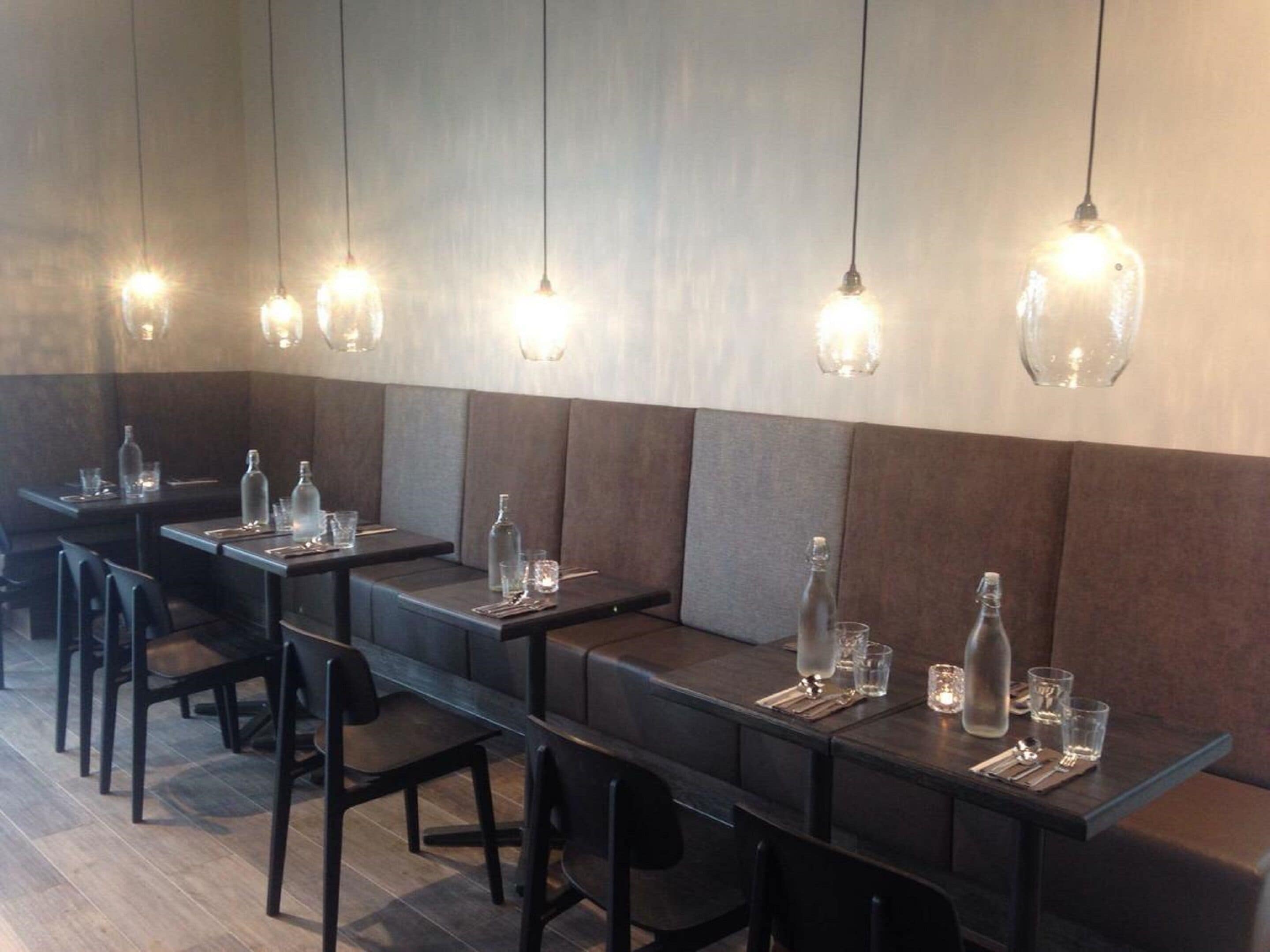 Interior de restaurante con mesas largas, sillas y lámparas colgantes.