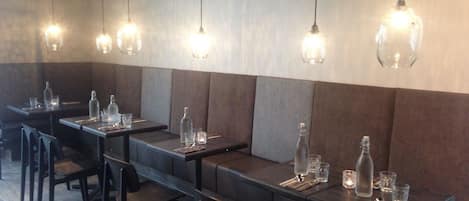 Interior de restaurante con mesas largas, sillas y lámparas colgantes.