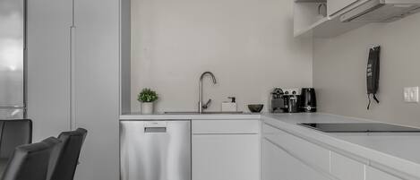 Uma cozinha moderna com armários brancos, máquina de lavar louça, pia e cafeteira.