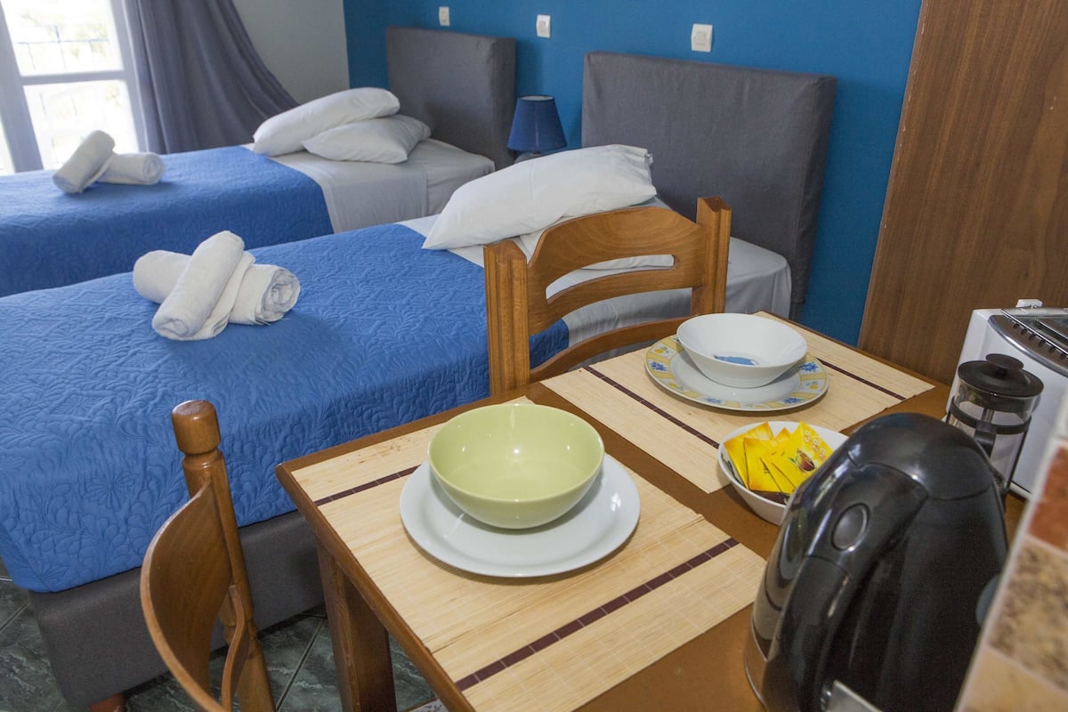 A hotel room with two beds, a dining table with a bowl and plates, and a coffee maker.