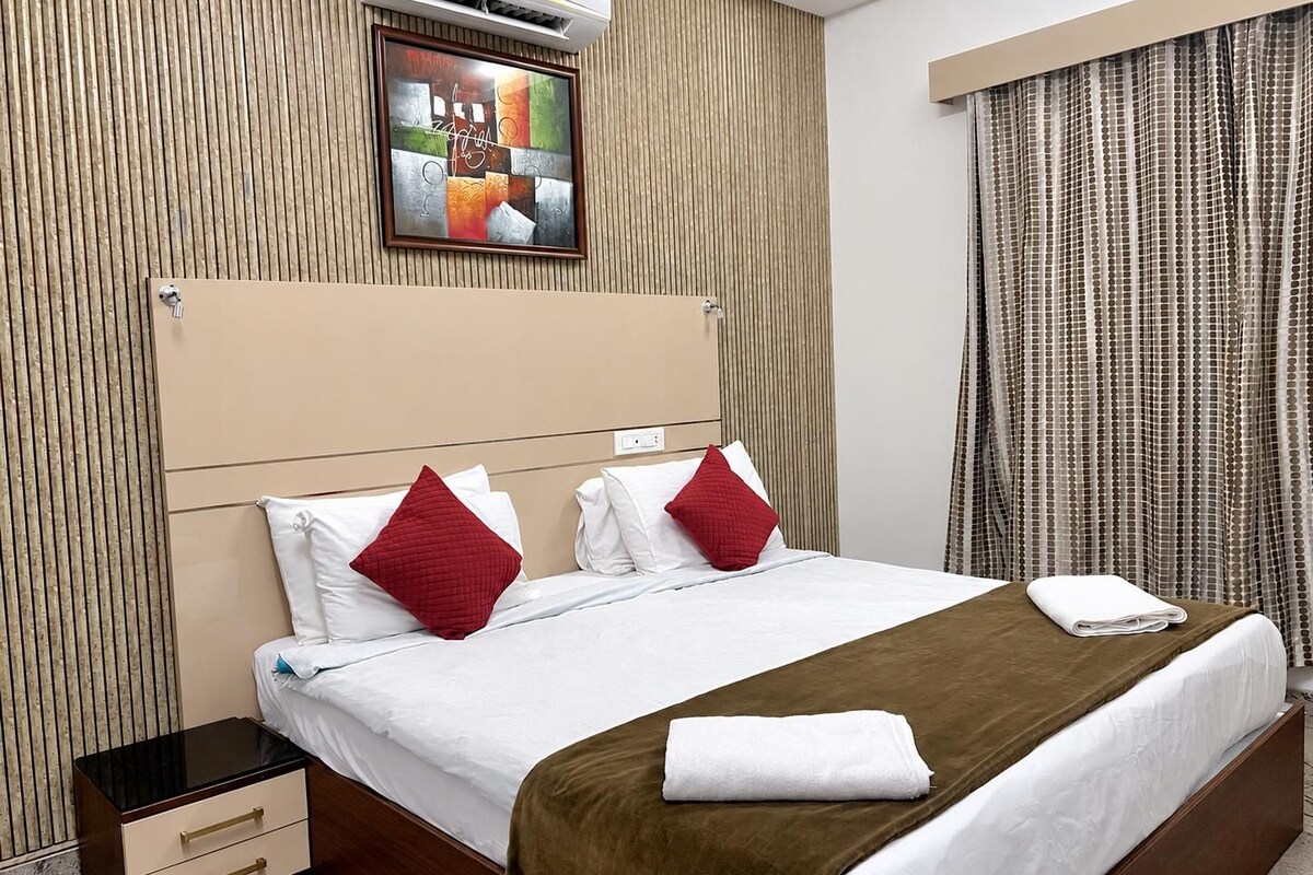 Una habitación de hotel con una cama, una mesita de noche, aire acondicionado instalado en la pared y una ventana con cortinas.