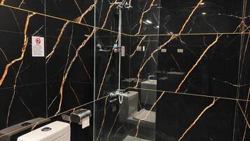 A modern bathroom with black marble walls, a glass shower enclosure, and a toilet.