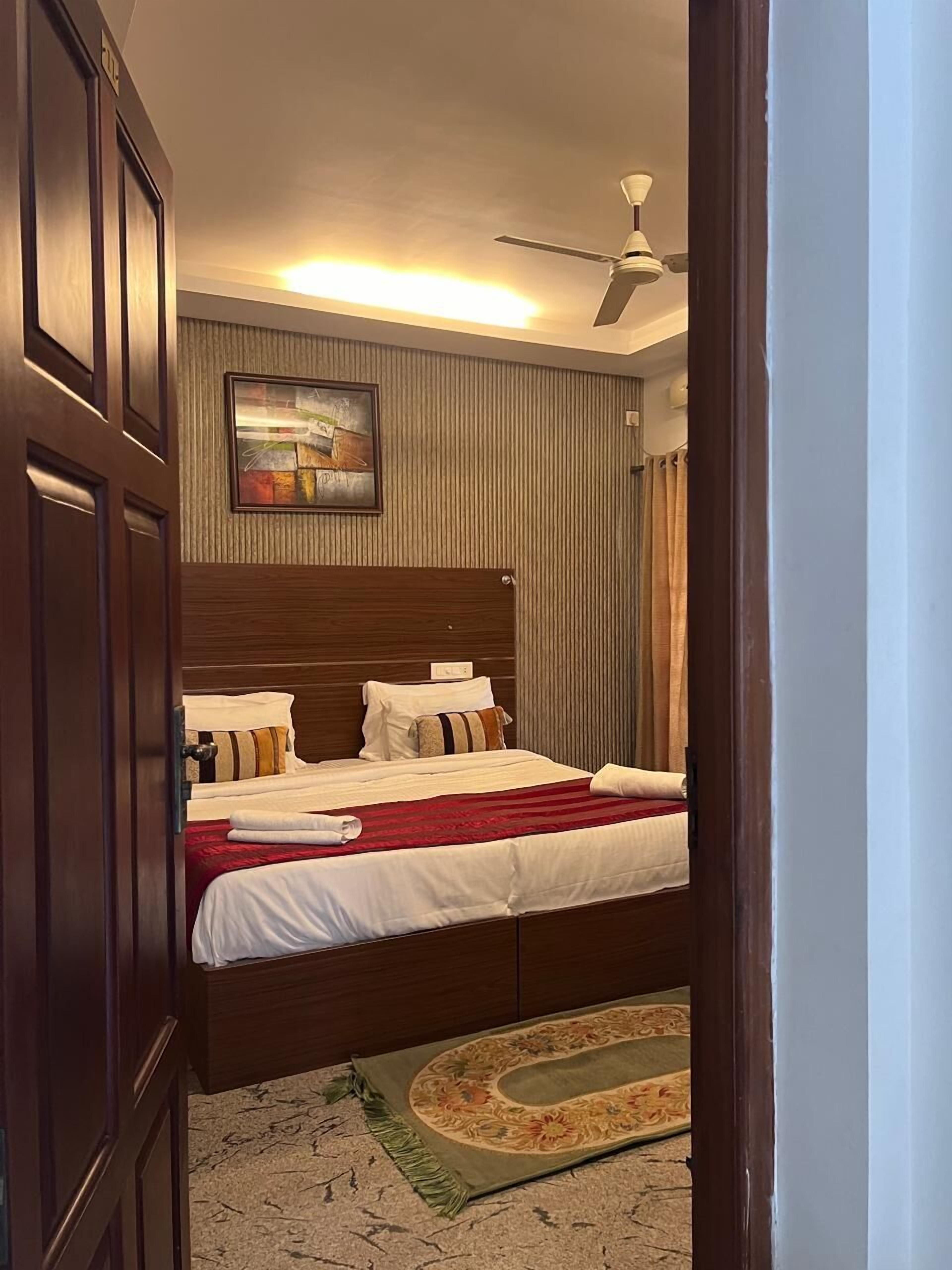 A hotel room with a wooden bed, a ceiling fan, a painting on the wall, and a patterned rug.