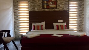 A hotel room with a stone wall, a wooden headboard, a bed with red bedding, two pillows, and a painting above the bed. - Fortkochi Beach Inn (Kochi)