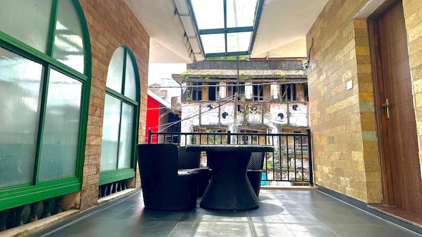 A covered outdoor area with a glass ceiling, wicker furniture, and a view of a multi-story building with graffiti. - Fortkochi Beach Inn (Kochi)
