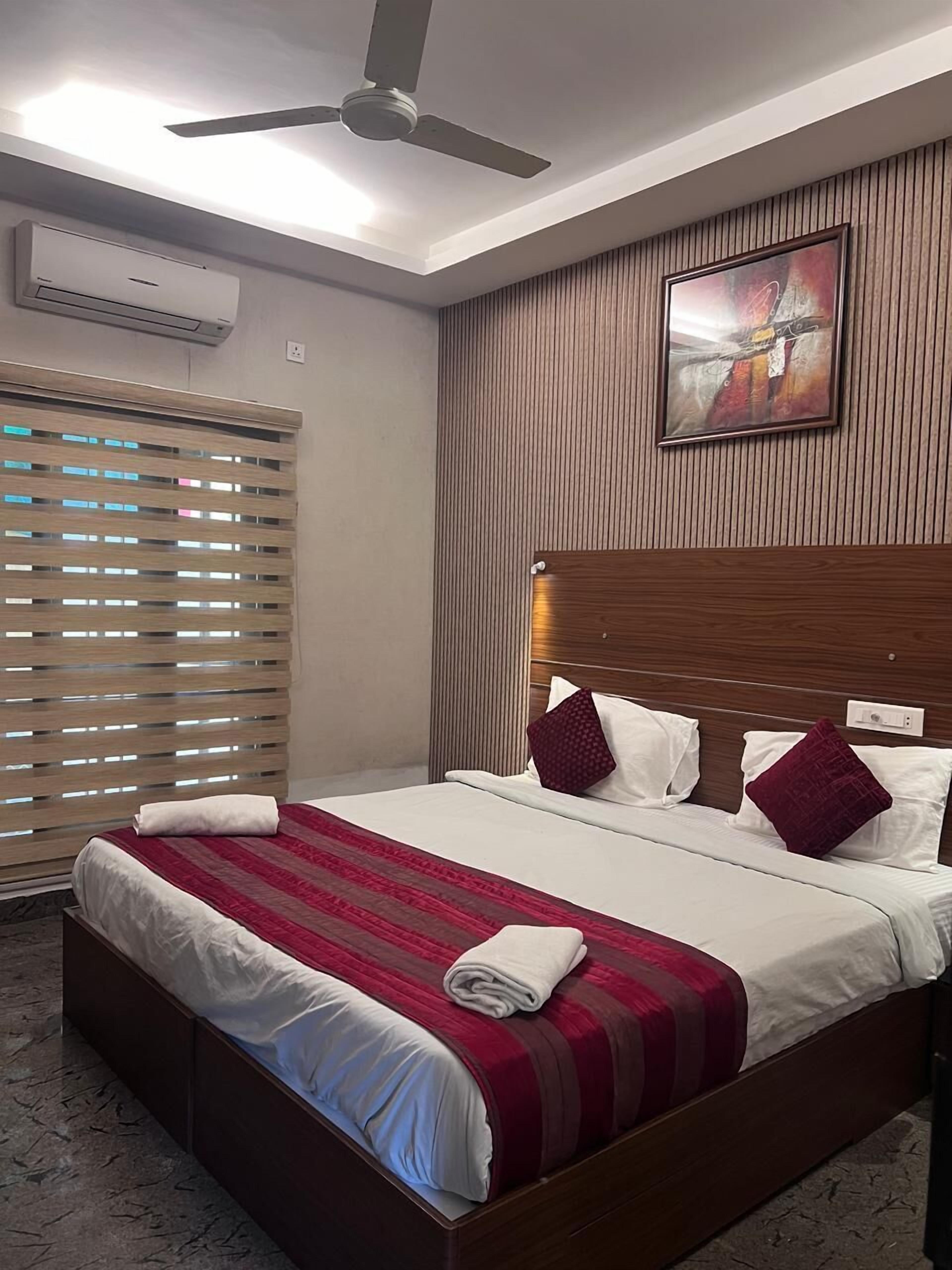 A hotel room with a large bed, a ceiling fan, an air conditioning unit, a wooden headboard, and a framed picture on the wall.