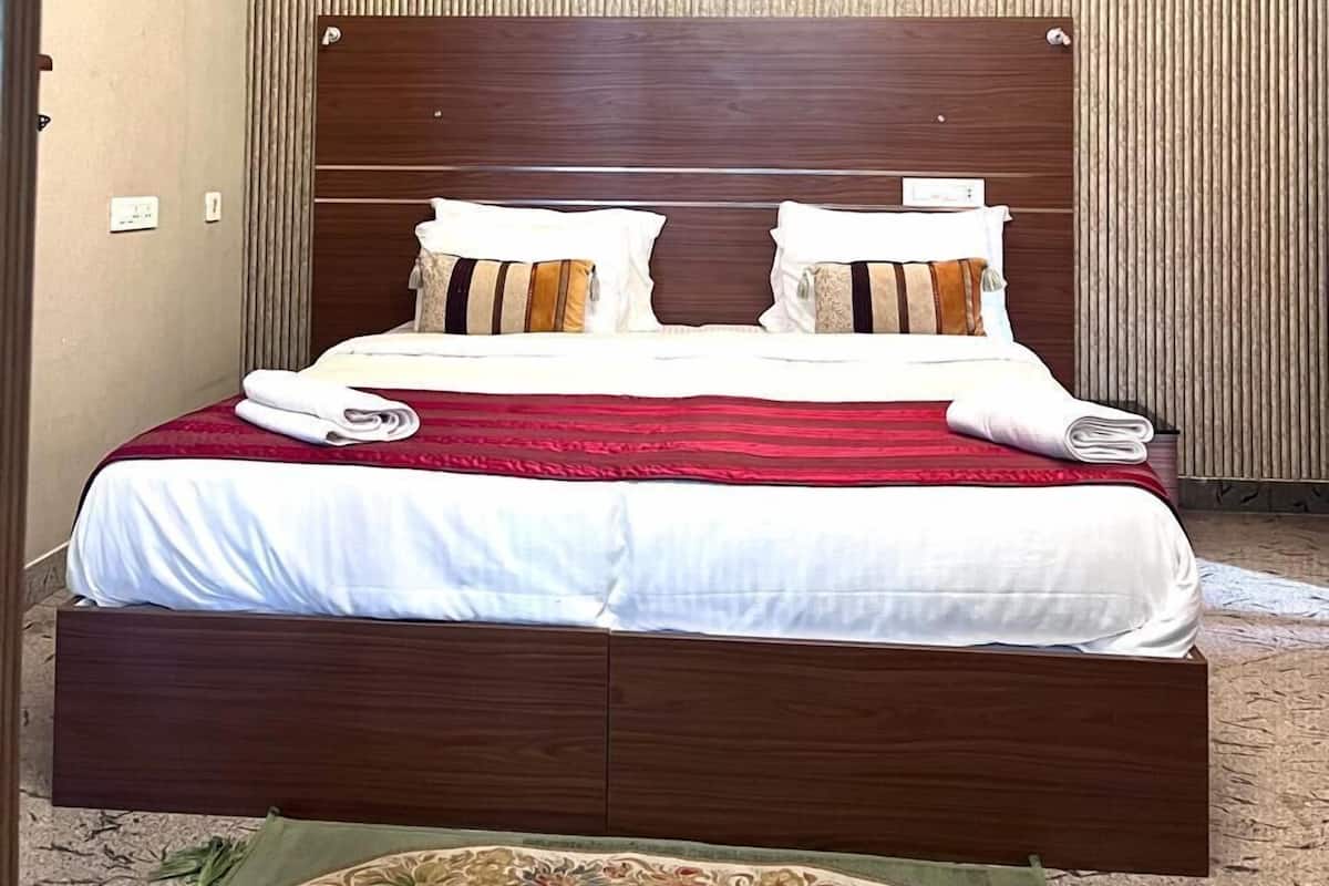 Ein ordentlich bezogenes Doppelbett mit einer rot-weißen Tagesdecke, zwei Kissen und einem gefalteten Handtuch. Über dem Bett ist ein Deckenventilator zu sehen.