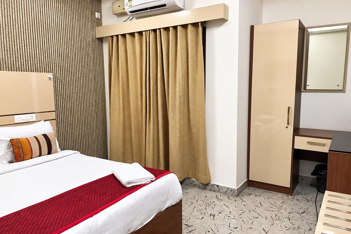 Habitación de hotel con cama, escritorio, armario, aire acondicionado y espejo.
