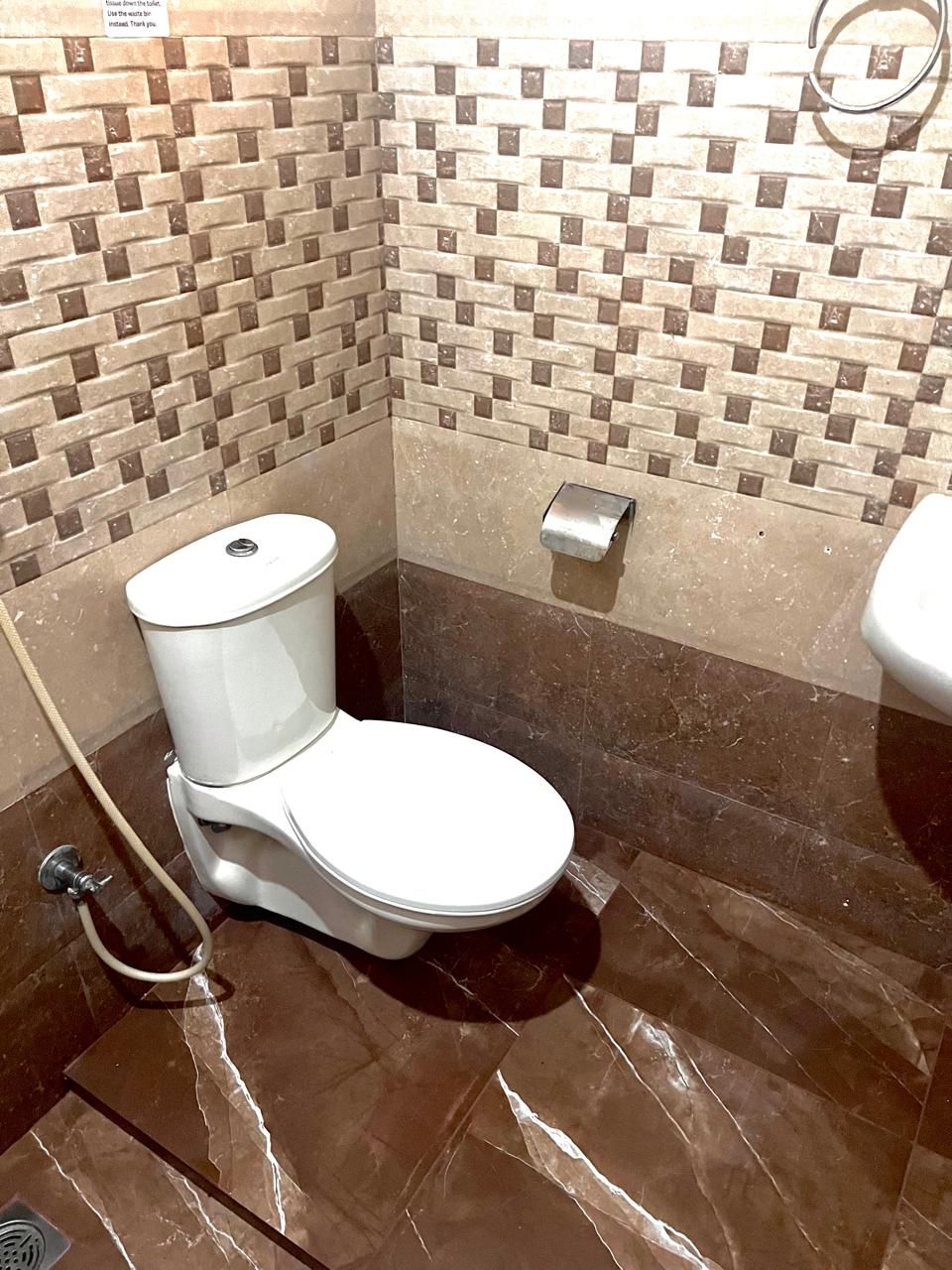 Une salle de bain équipée de toilettes, d’un sèche-mains et d’un mur recouvert de carreaux.