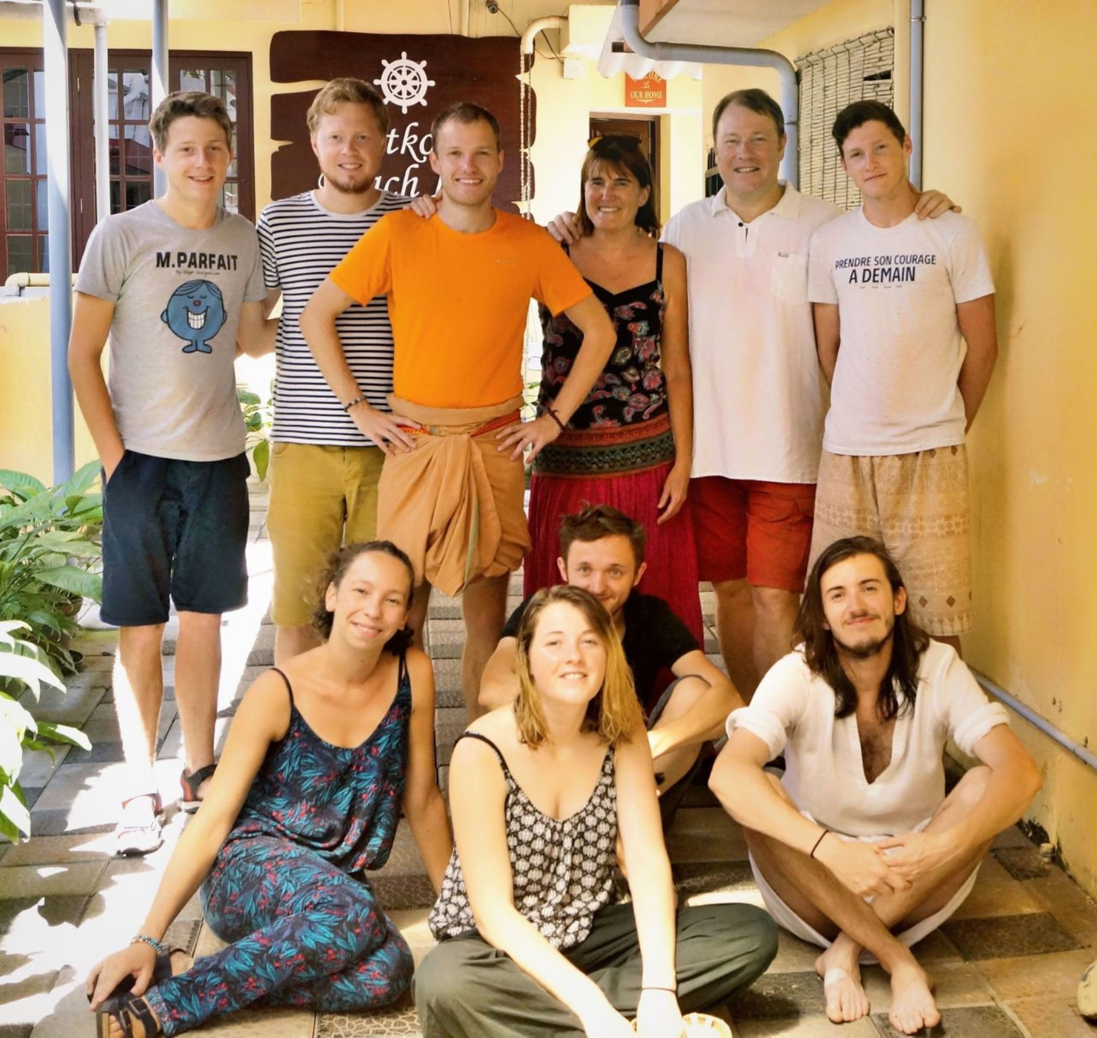 A group of people standing and sitting in an outdoor area with a yellow wall and a door labeled "Our Home".