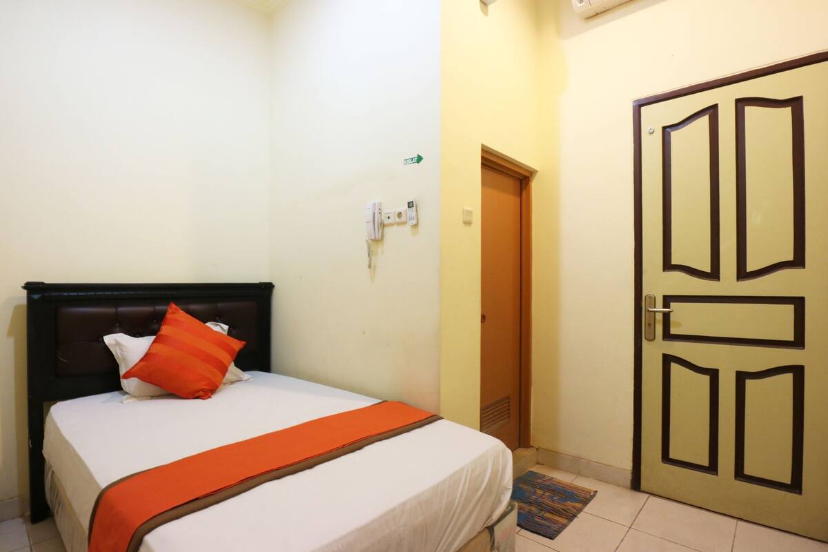 A bedroom with a bed, a door, and a wall-mounted light switch.