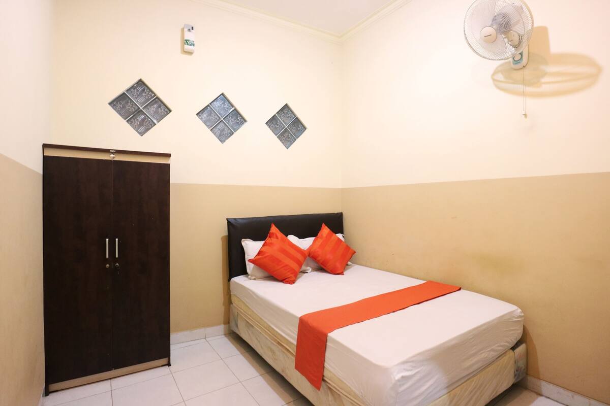 A bedroom with a bed, a wardrobe, and a wall-mounted fan.