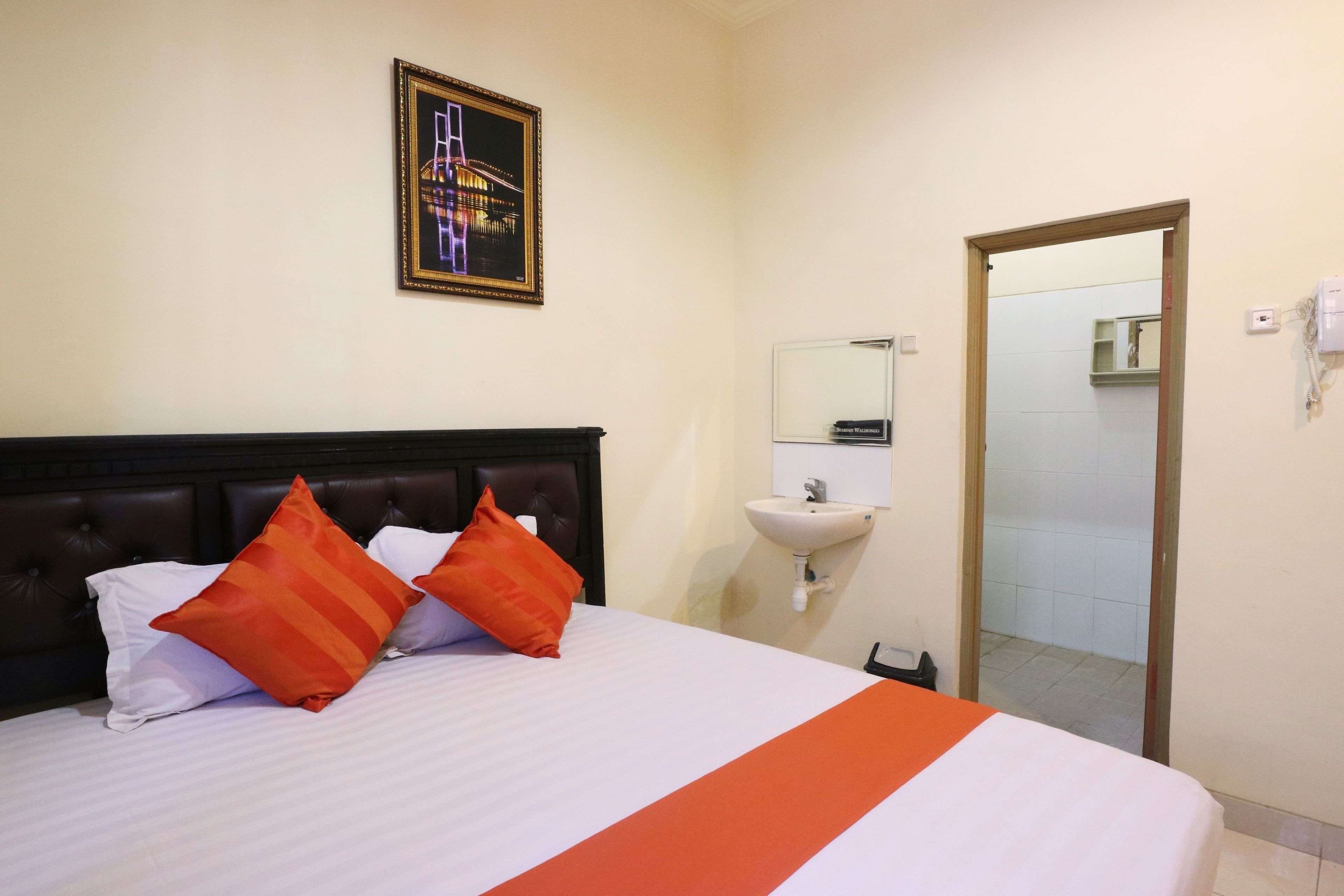 A hotel room with a bed, a nightstand, a mirror, and a bathroom visible through an open door.