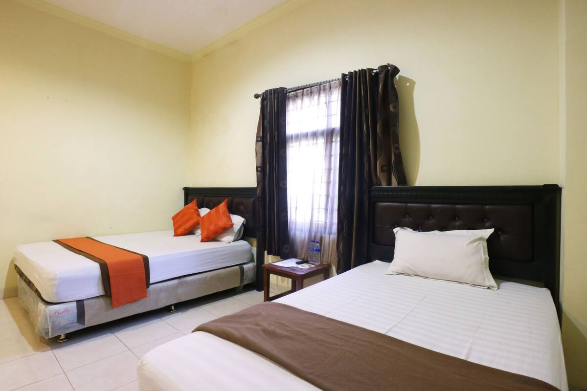 A hotel room with two beds, one with a brown blanket and the other with an orange blanket.