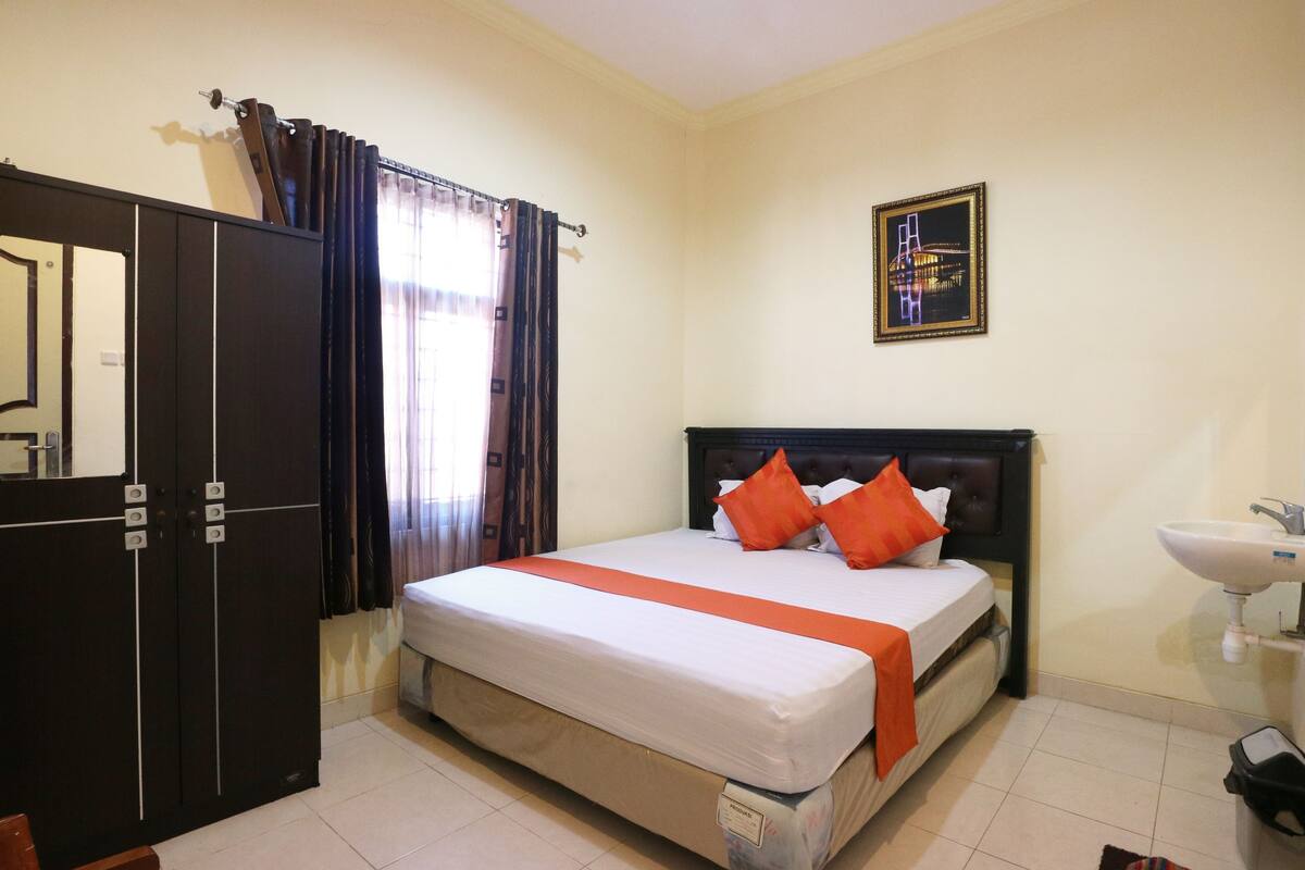 A hotel room with a bed, a wardrobe, a bathroom with a sink, and a framed picture on the wall.