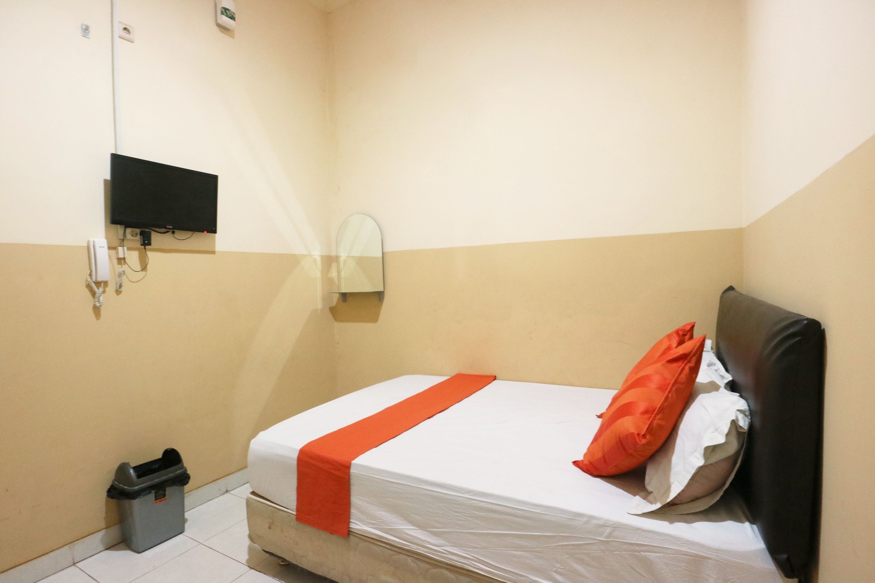 Una habitación pequeña y limpia con una cama individual, un televisor montado en la pared y un cubo de basura.