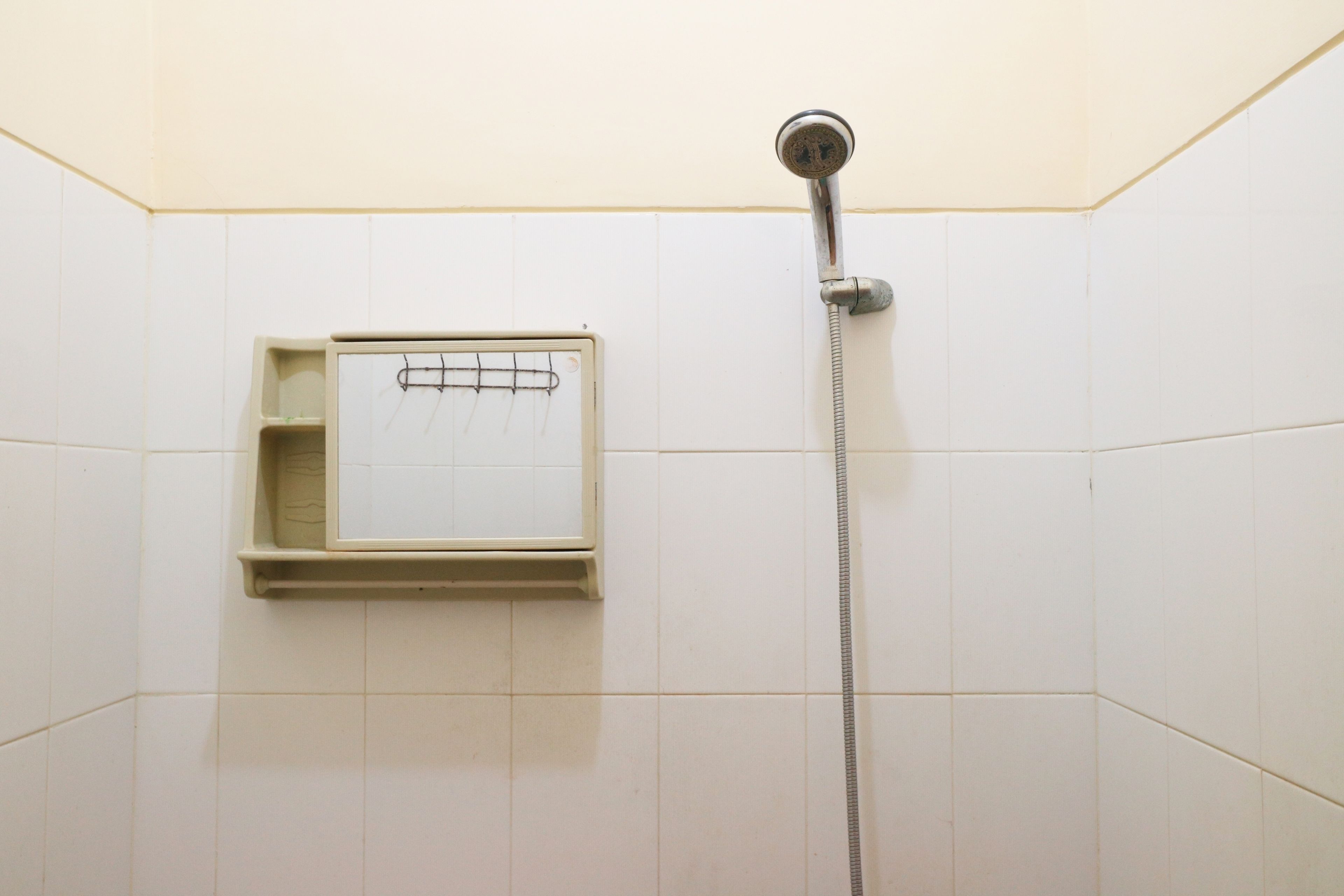 A shower with a handheld showerhead and a small shelf with a mirror.