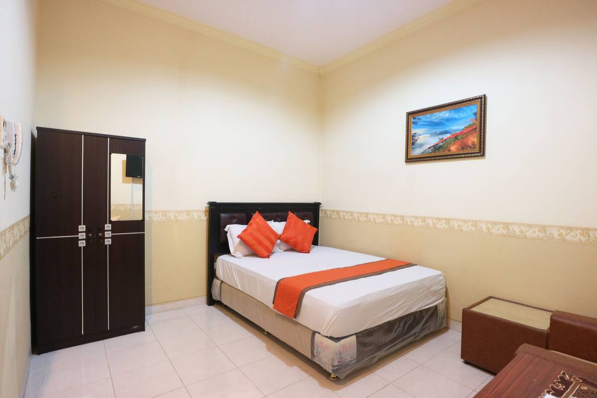 A bedroom with a bed, a wardrobe, a painting on the wall, and a small table.