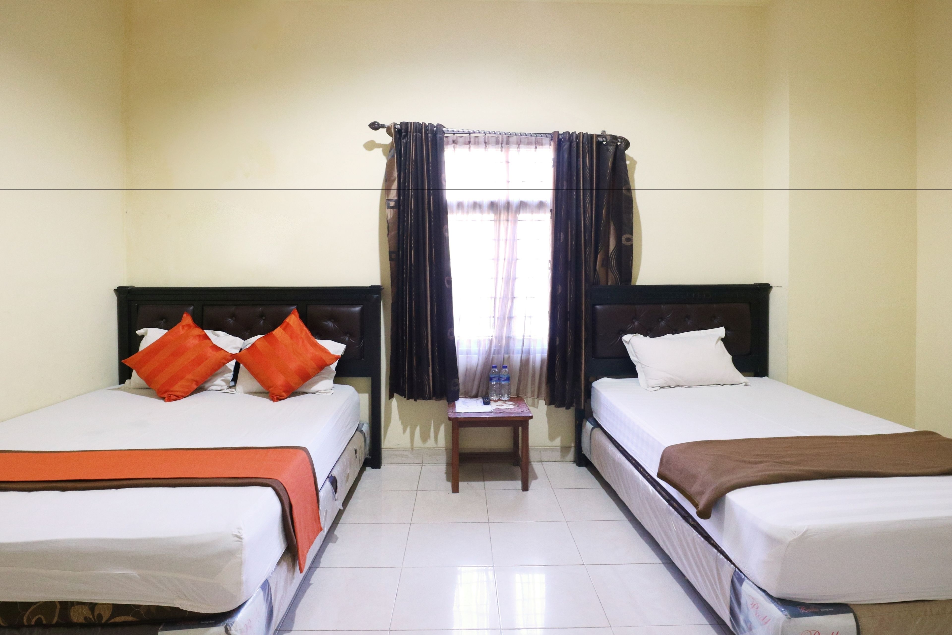 A hotel room with two single beds, a small wooden table, and a window with curtains.