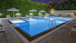 Una piscina rectangular con plataforma de baldosas, rodeada de sillones de descanso y sombrillas.