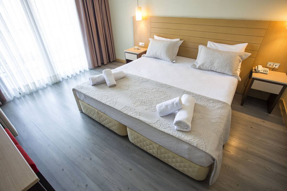 A hotel room with a large bed, bedside tables, a bedside lamp, and a telephone.