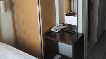 Habitación de hotel con cama, armario de madera, escritorio con teléfono y control remoto, espejo y puerta que da a otra habitación.
