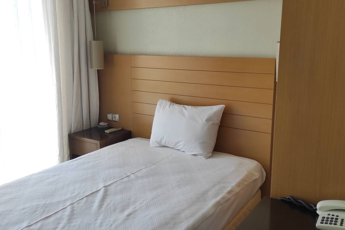A hotel room with a bed, a nightstand, a telephone, and an air conditioning unit.