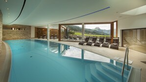 Piscina interna con vista chiara sulle montagne, sedie a sdraio e un muro in pietra.