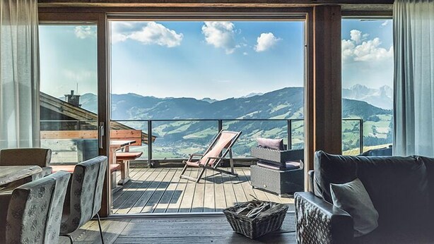 Un balcone con pavimento in legno, una poltrona imbottita, un tavolino e un cesto in vimini.