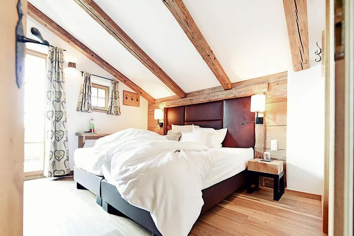 Un dormitorio con una cama grande, vigas de madera, una mesita de noche y una mesilla auxiliar.
