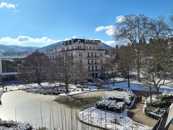 Un edificio grande e histórico con varios balcones, un patio cubierto de nieve y un estanque congelado.