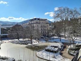 Un edificio grande e histórico con varios balcones, un patio cubierto de nieve y un estanque congelado.