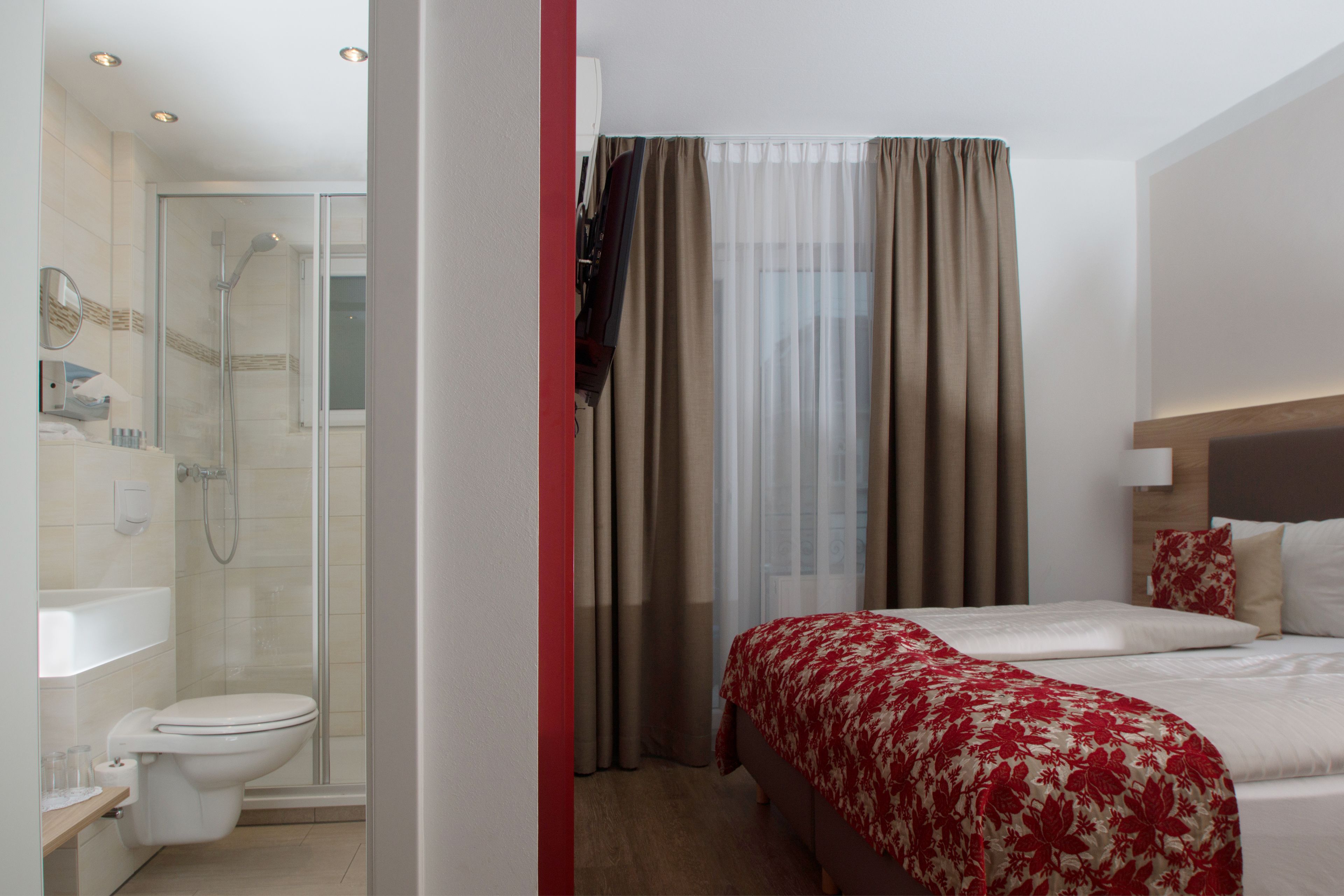 Una habitación de hotel con ducha, inodoro y cama con colcha estampada.