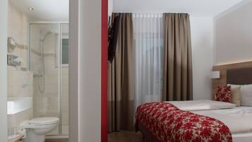 A hotel room with a shower, toilet, and a bed with a floral bedspread.