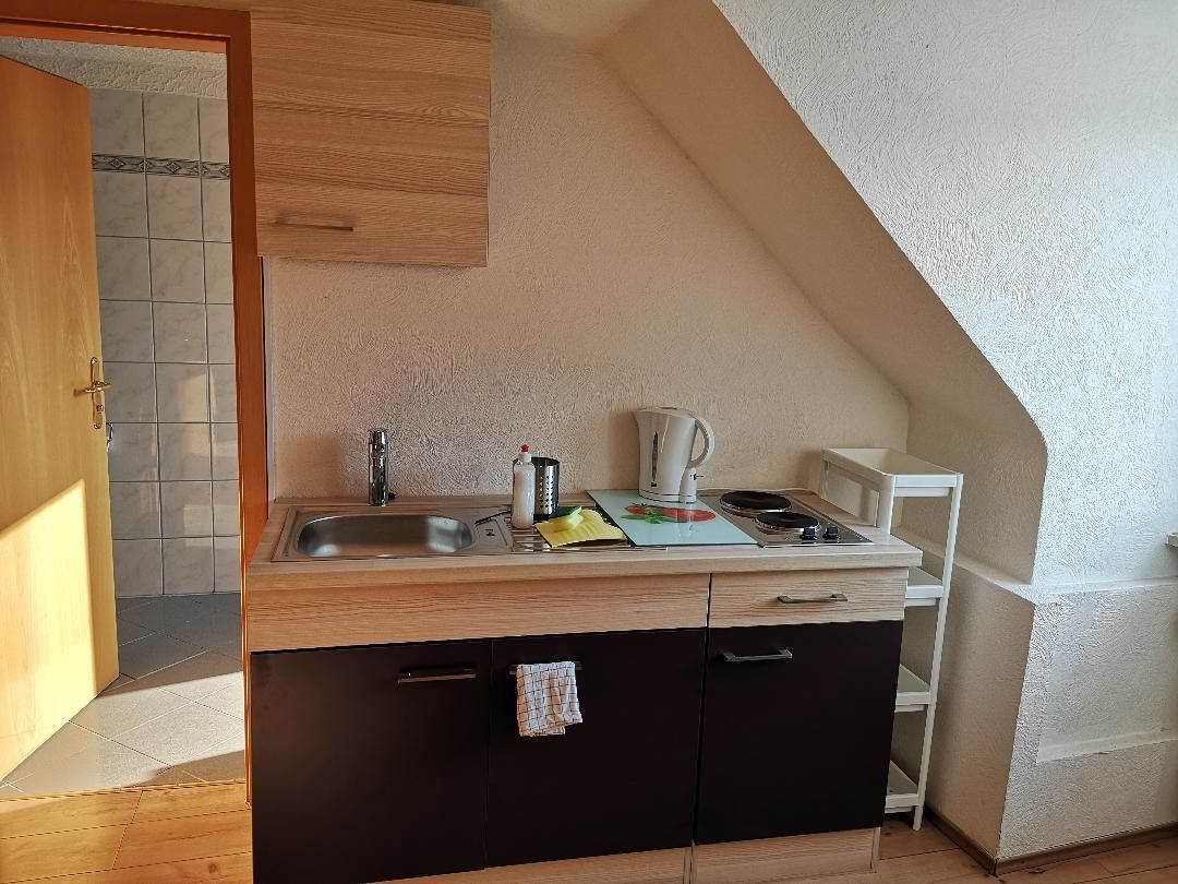 A compact kitchen with a wooden countertop, a sink, a kettle, and a microwave.