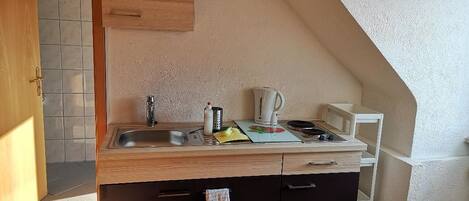 A compact kitchen with a wooden countertop, a sink, a kettle, and a microwave.