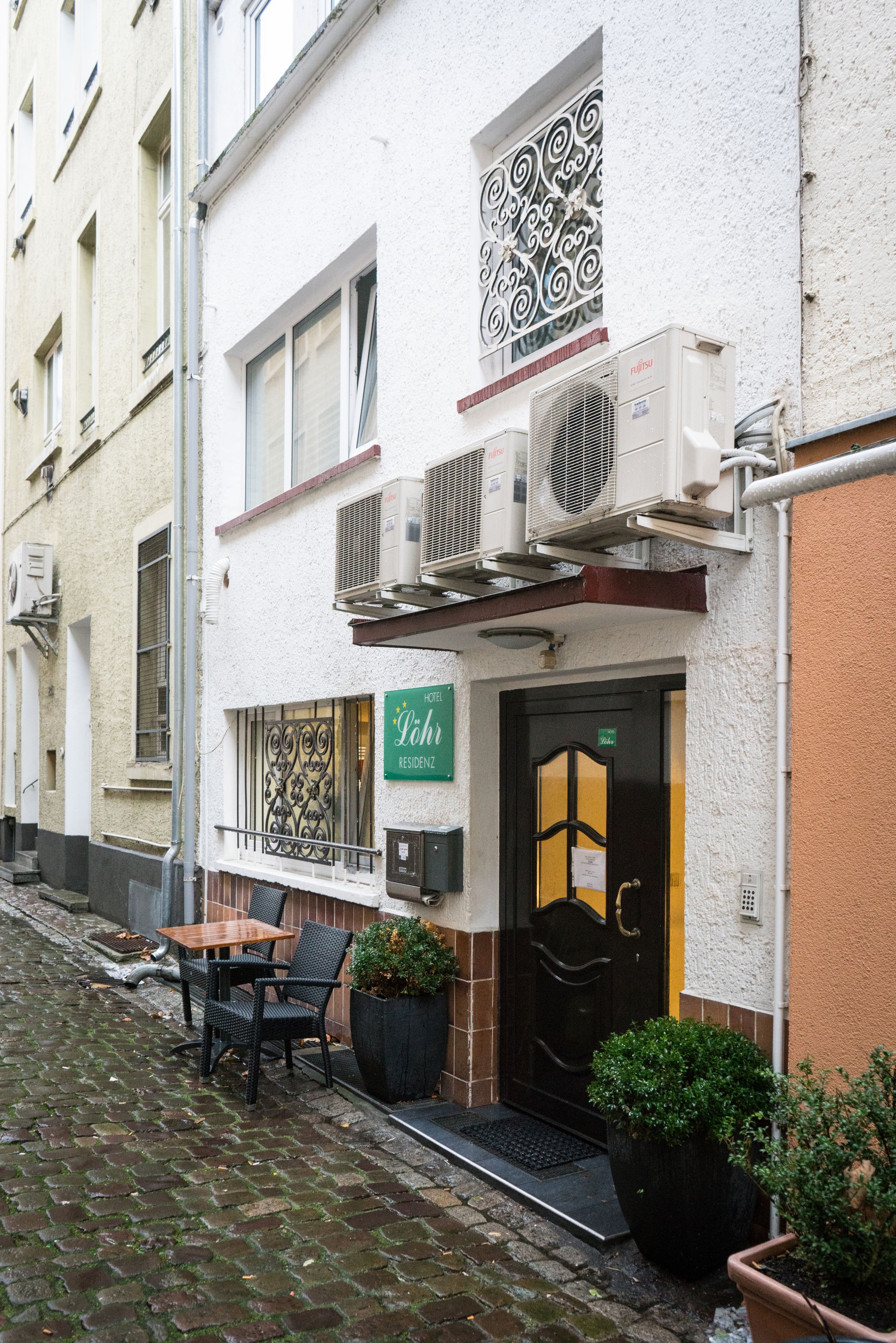 A hotel entrance with a sign reading "Hotel Lahr" and a black door. There are outdoor seating with chairs and a table, and potted plants near the entrance.