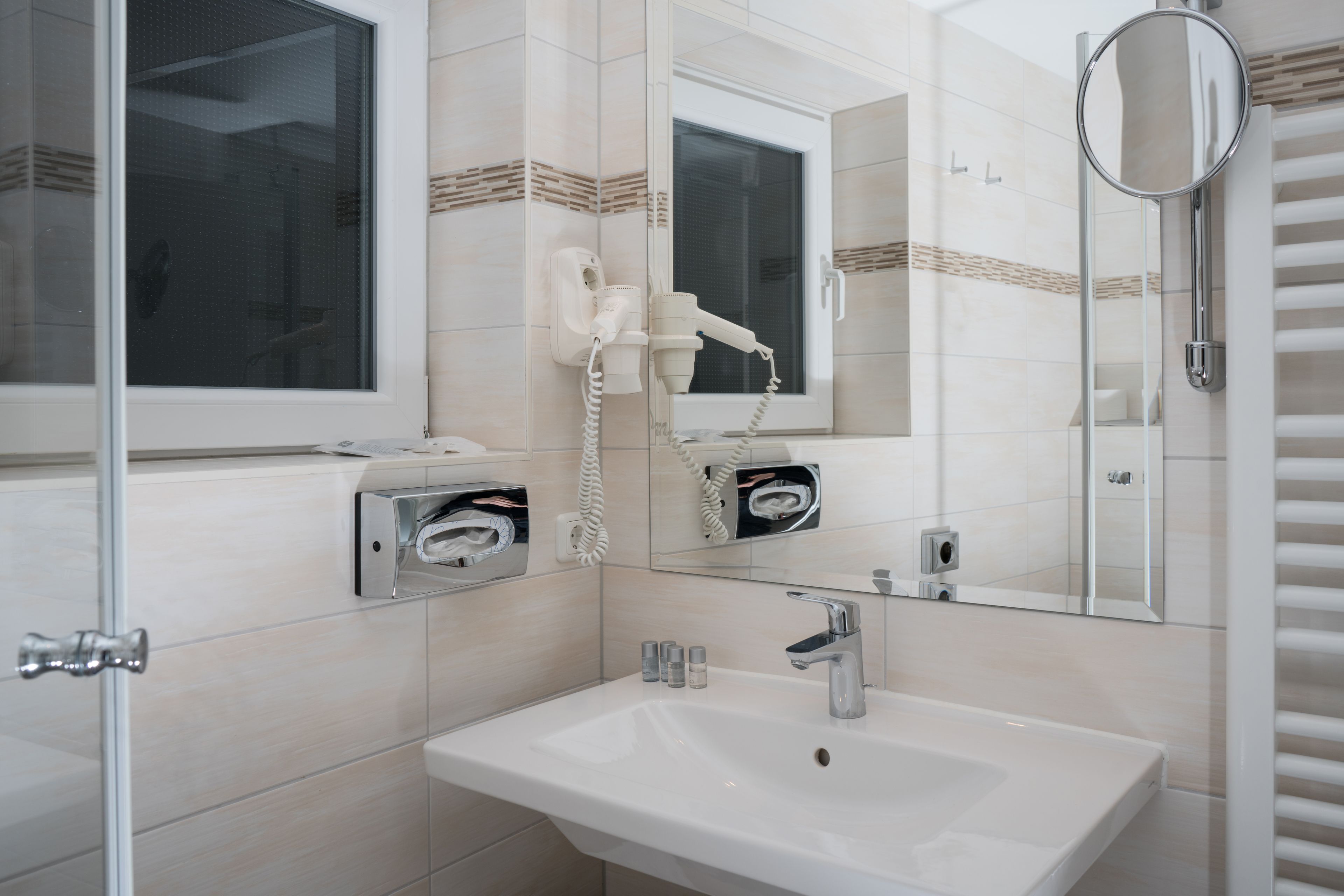 Ein modernes Badezimmer mit einem weißen Waschbecken, einem Spiegel, einem Fön und einer Dusche.