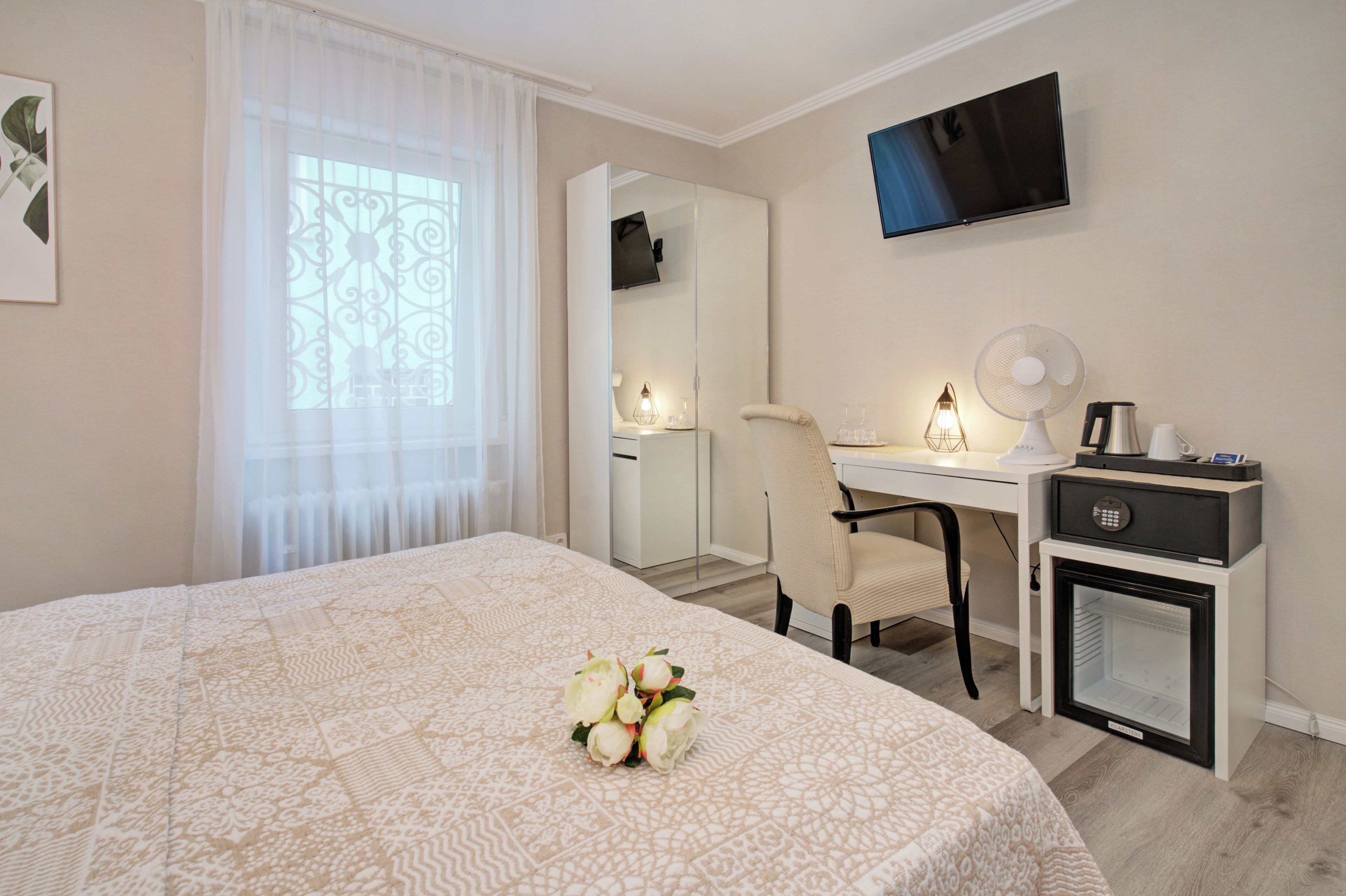 A hotel room with a bed, a desk, a chair, a TV, a fan, and a mini-fridge.