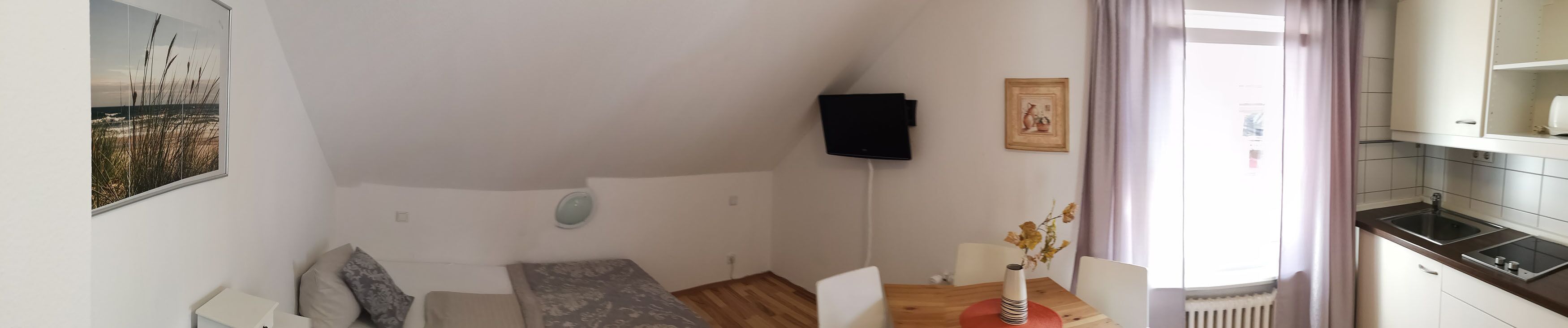 A bedroom with a bed, a bedside table, a wall-mounted TV, and a window with curtains.