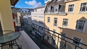 Un balcon doté d’une table et de chaises en verre, offrant une vue sur une rangée d’immeubles avec de nombreuses fenêtres et balcons.