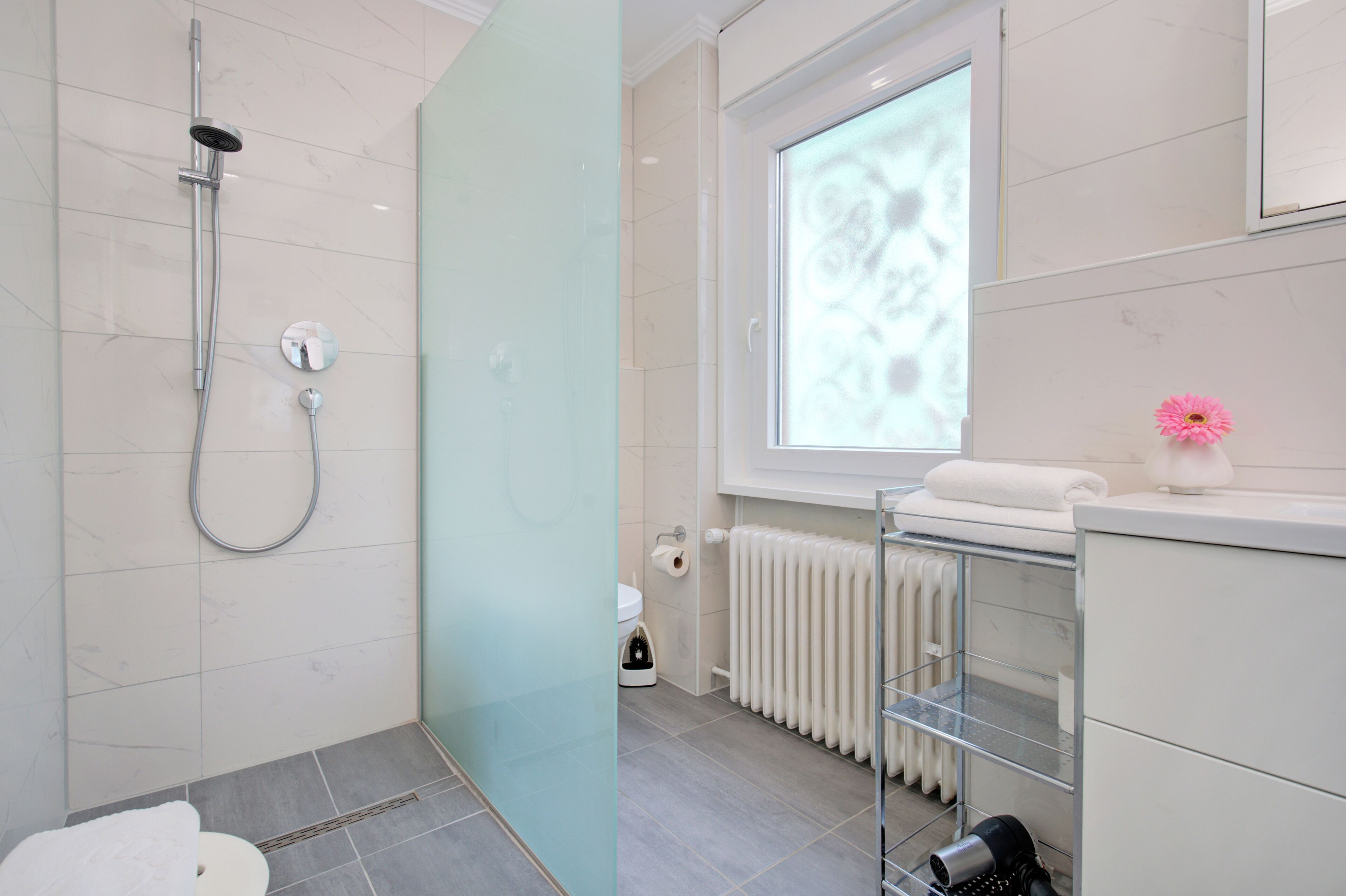 A modern bathroom with a glass shower enclosure, a toilet, a radiator, and a window with a view.