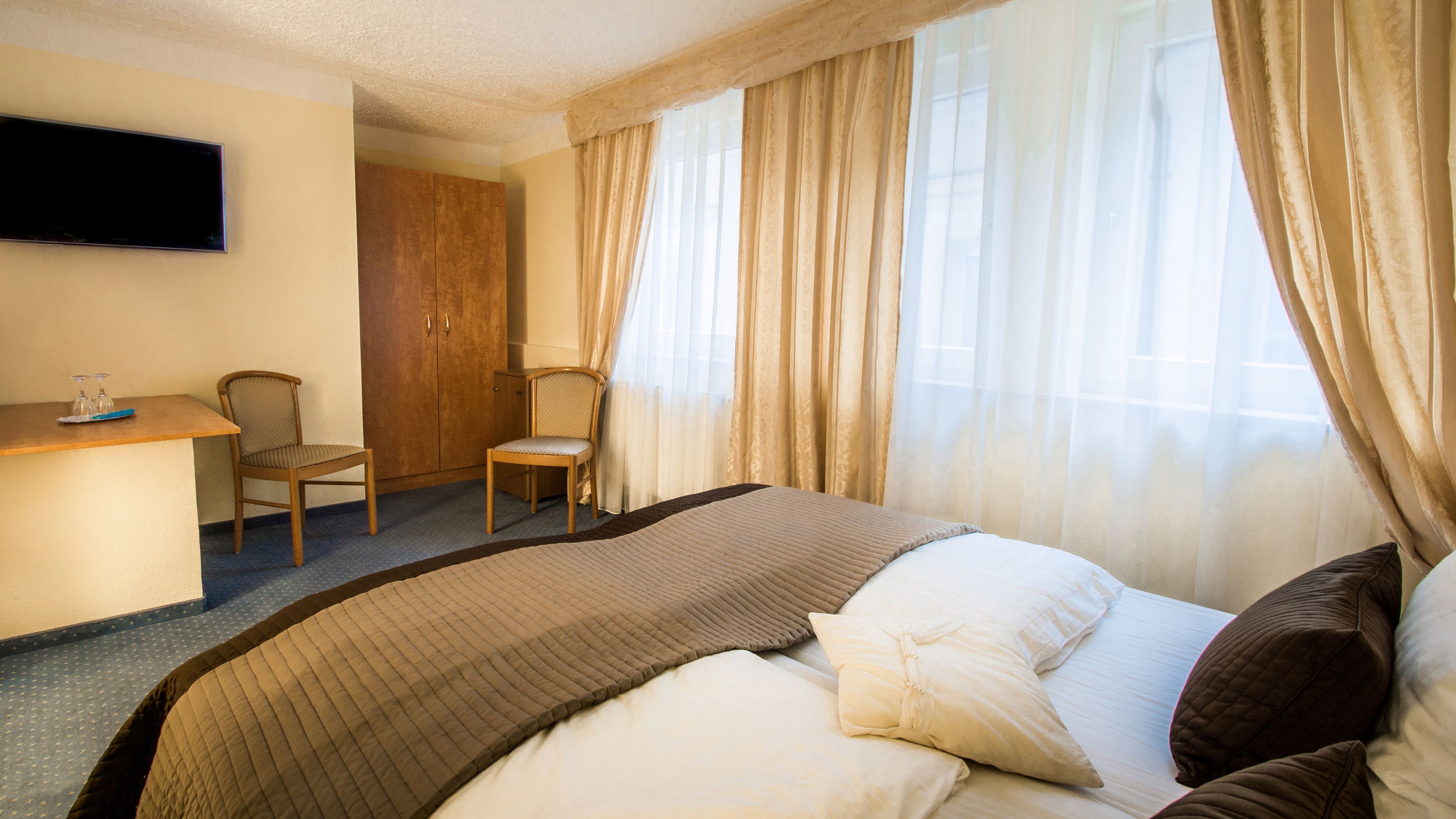 A hotel room with a bed, a desk, a chair, and a television on the wall.