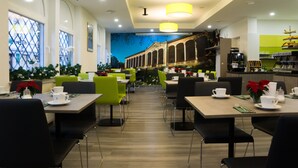 Un espace repas moderne avec des tables et des chaises, un coin cuisine et une fresque décorative sur le mur.
