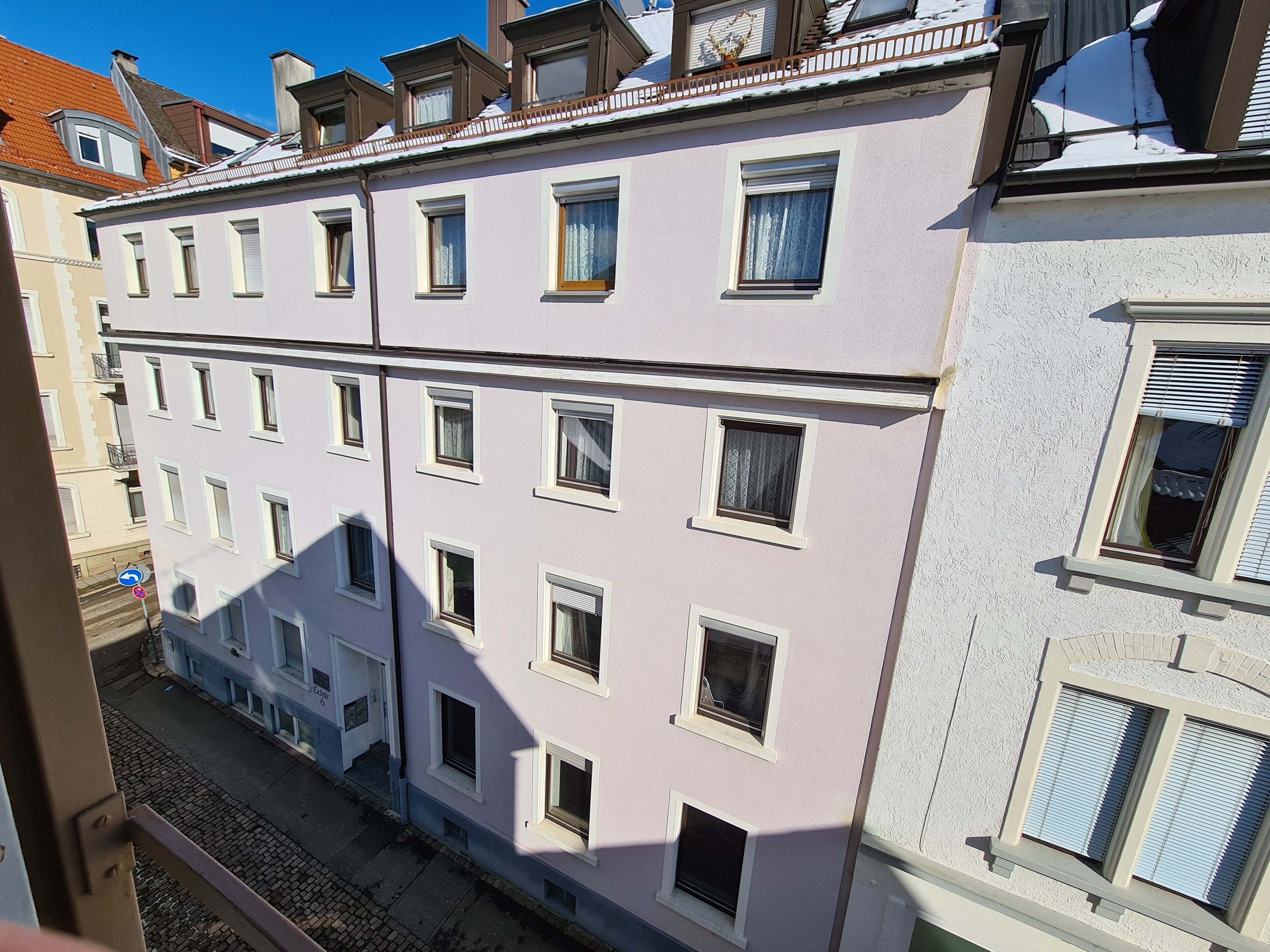 Een meerlaags gebouw met een rij ramen op de begane grond, een balkon met een hekwerk, en een zichtbare deur.