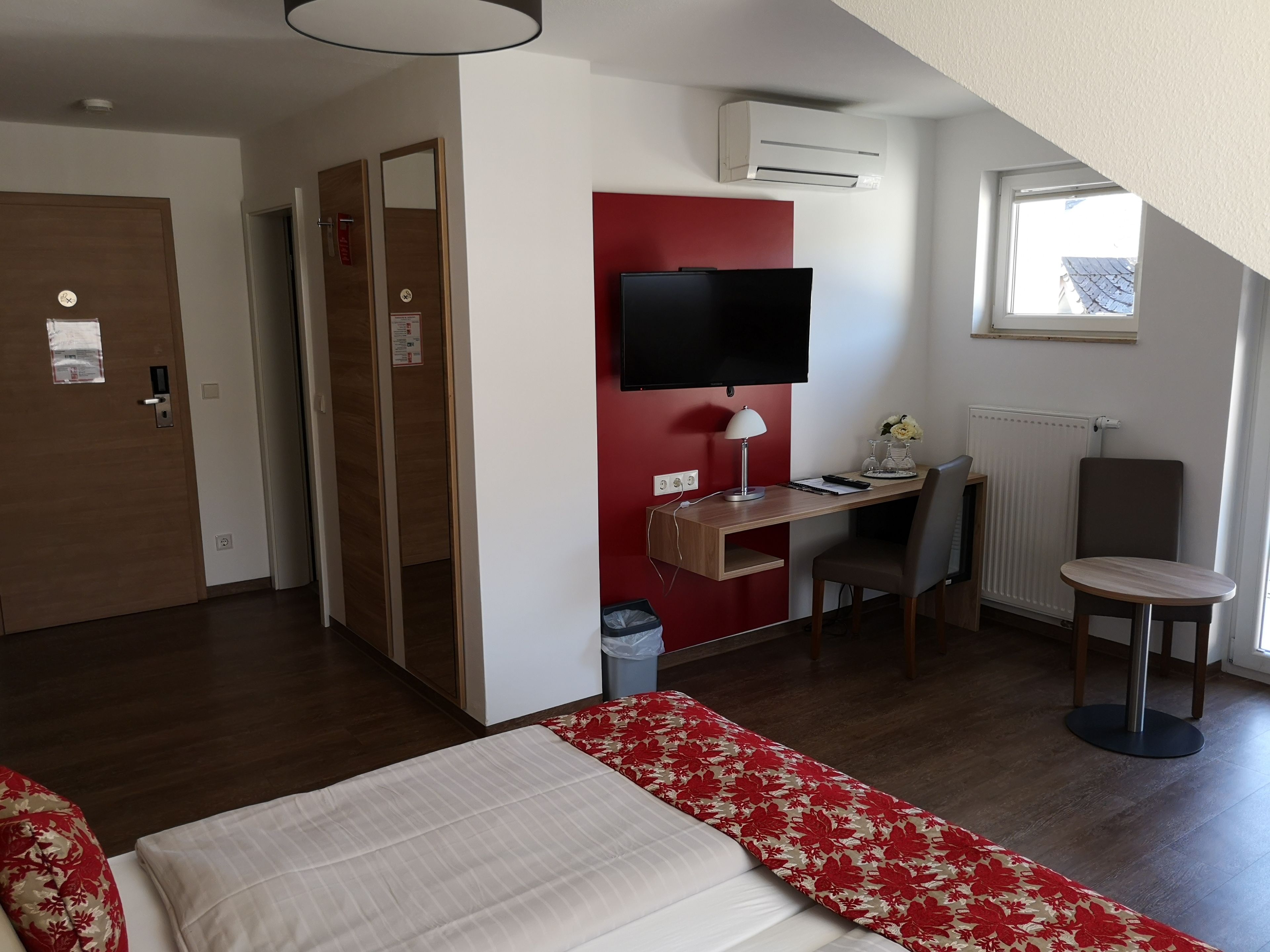 A hotel room with a bed, a desk with a computer, a chair, a TV, and a window.