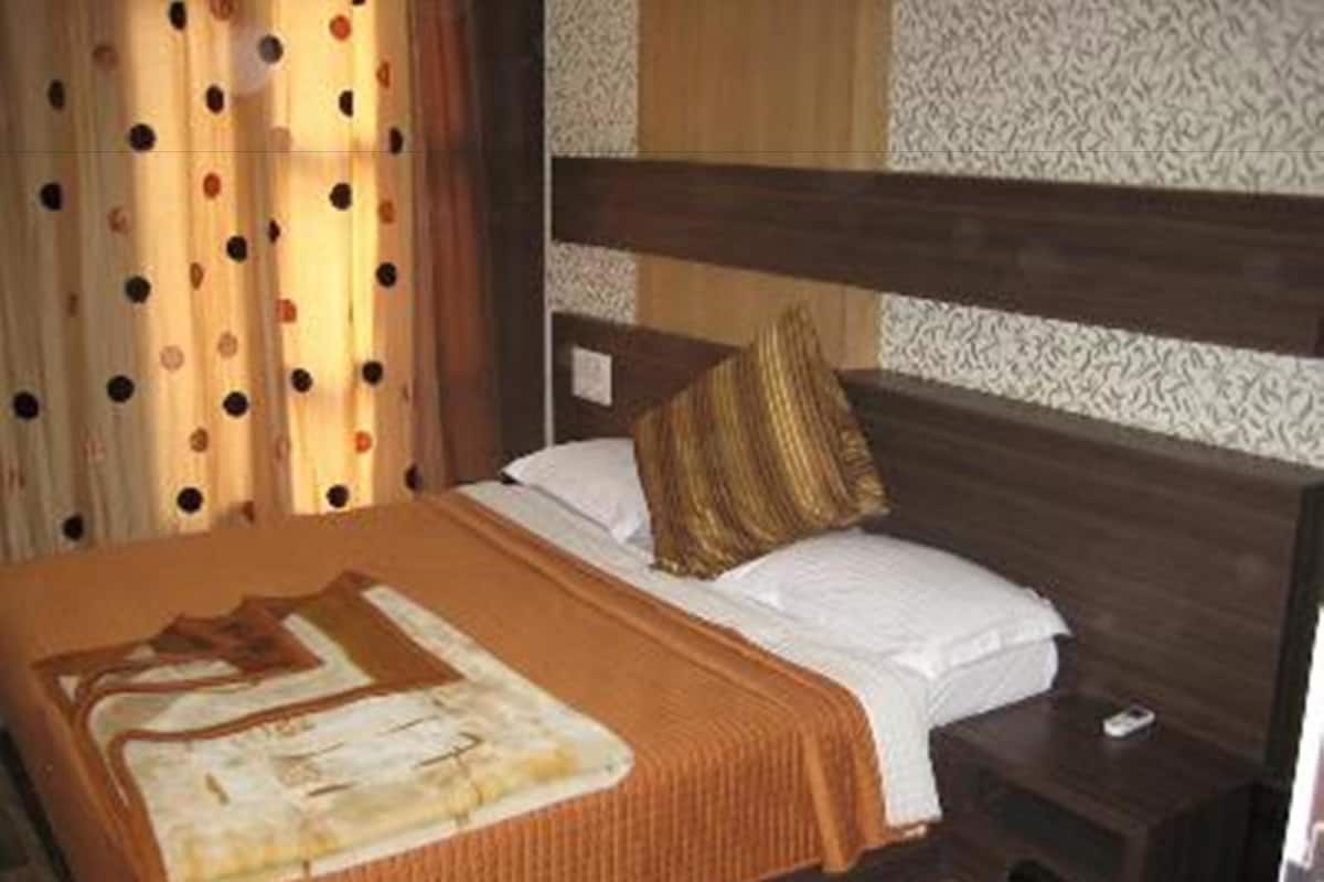 A hotel room with a large bed, a wooden headboard, a patterned wall, and a curtain with polka dots.