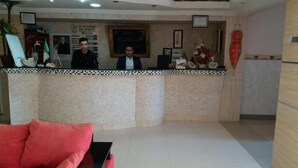 Zona de recepción de un hotel con mostrador, un sofá rojo y un cuadro en la pared.