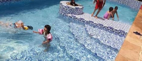Una piscina con escalones azulejados y una palmera.