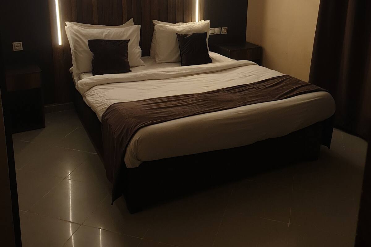 A modern bedroom with a large bed, dark wood paneling, and vertical light strips.